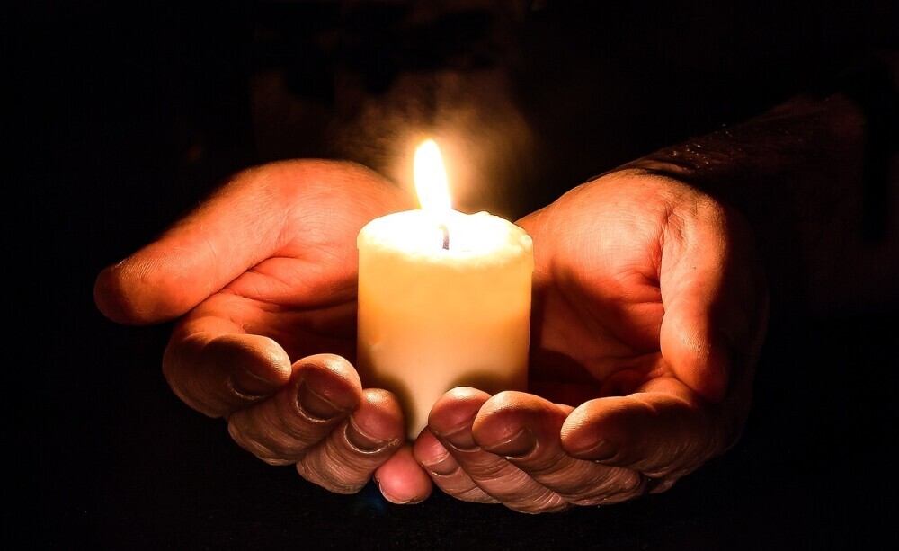 Image of a glowing candle ling placed on the hands of a man to show that there is hope in every struggle of loneliness life.