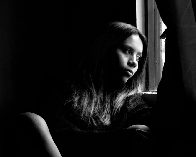 image of a lonely young girl staring out the window thinking wondering when will this loneliness end.