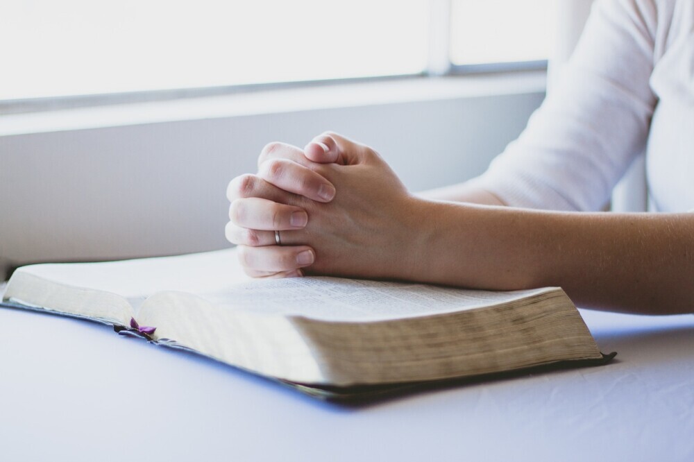 image of a person resting their folded hand on the Bible reflecting on God's promises in their loneliness.