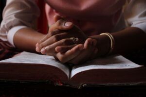 Close-up of a person praying with hands clasped over an open Bible, highlighting devotion.