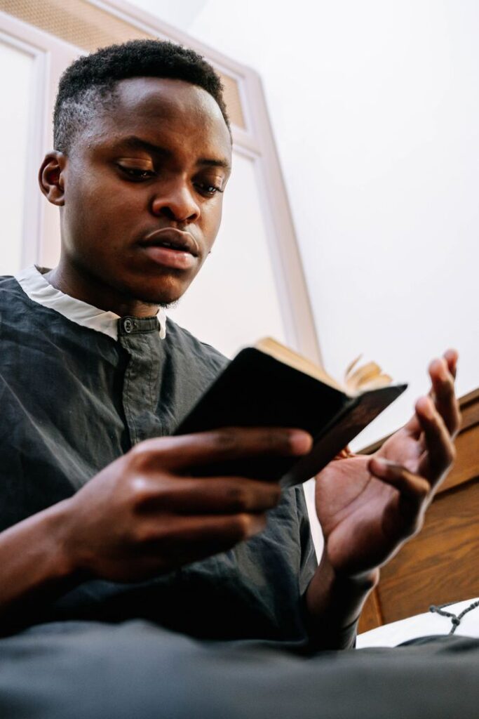 A young man in a religious outfit reads a Bible indoors, focused and meditative.