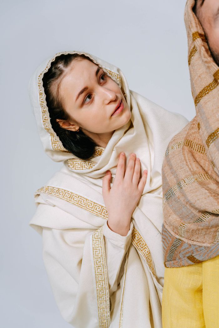 Portrait of a woman in a detailed traditional cloak and headscarf, gazing contemplatively.